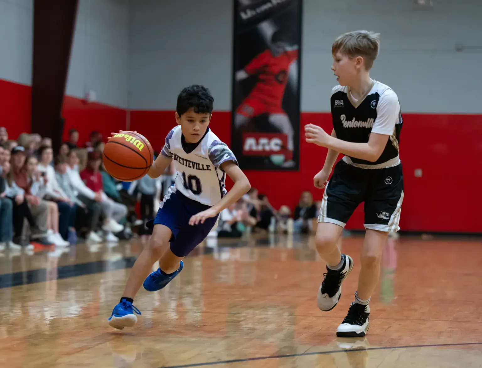 Boy dribbles a basketball, pursued by another boy on a court.