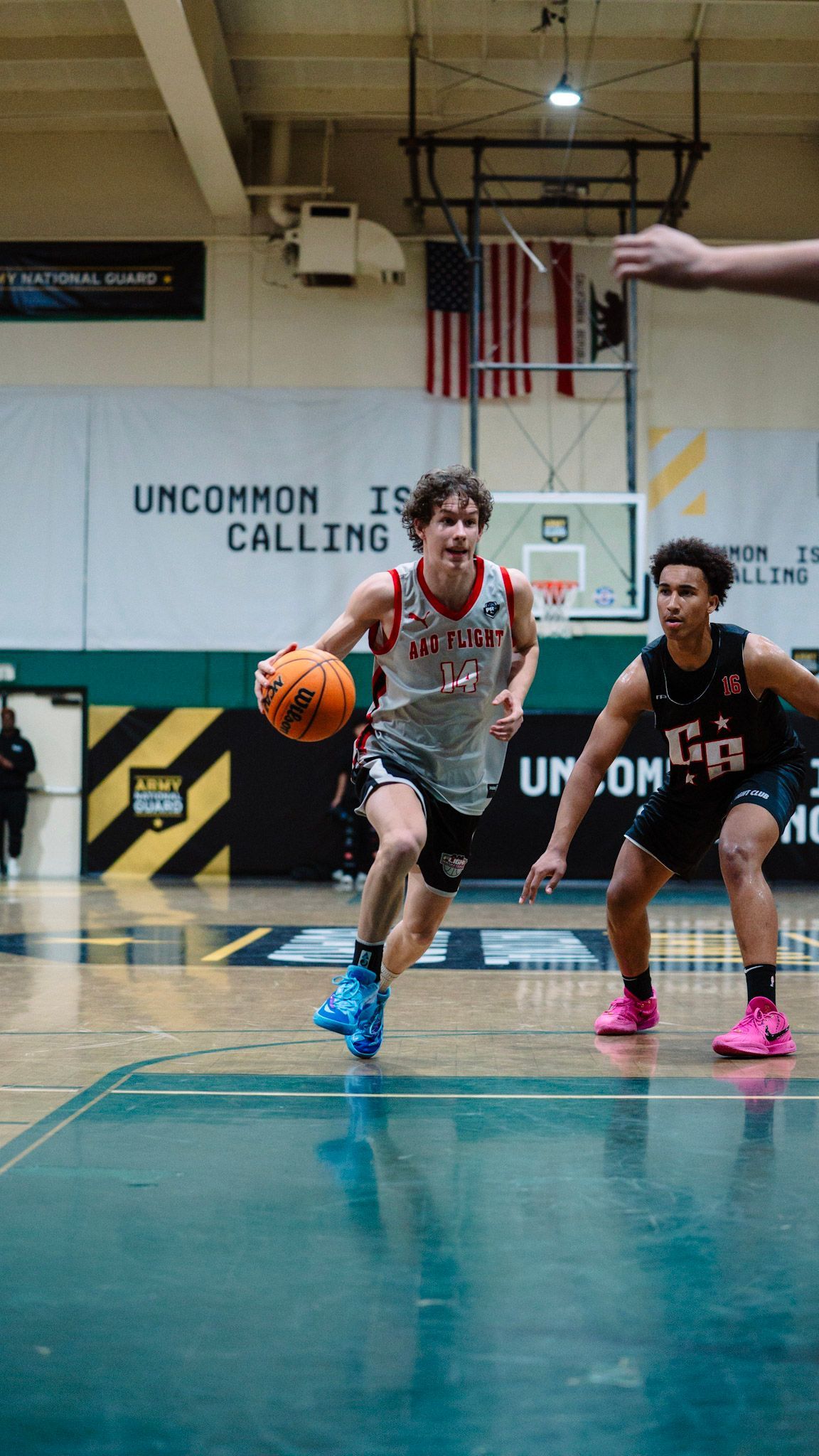 Basketball player dribbles orange ball, driving towards the basket. Opponent defends on court.