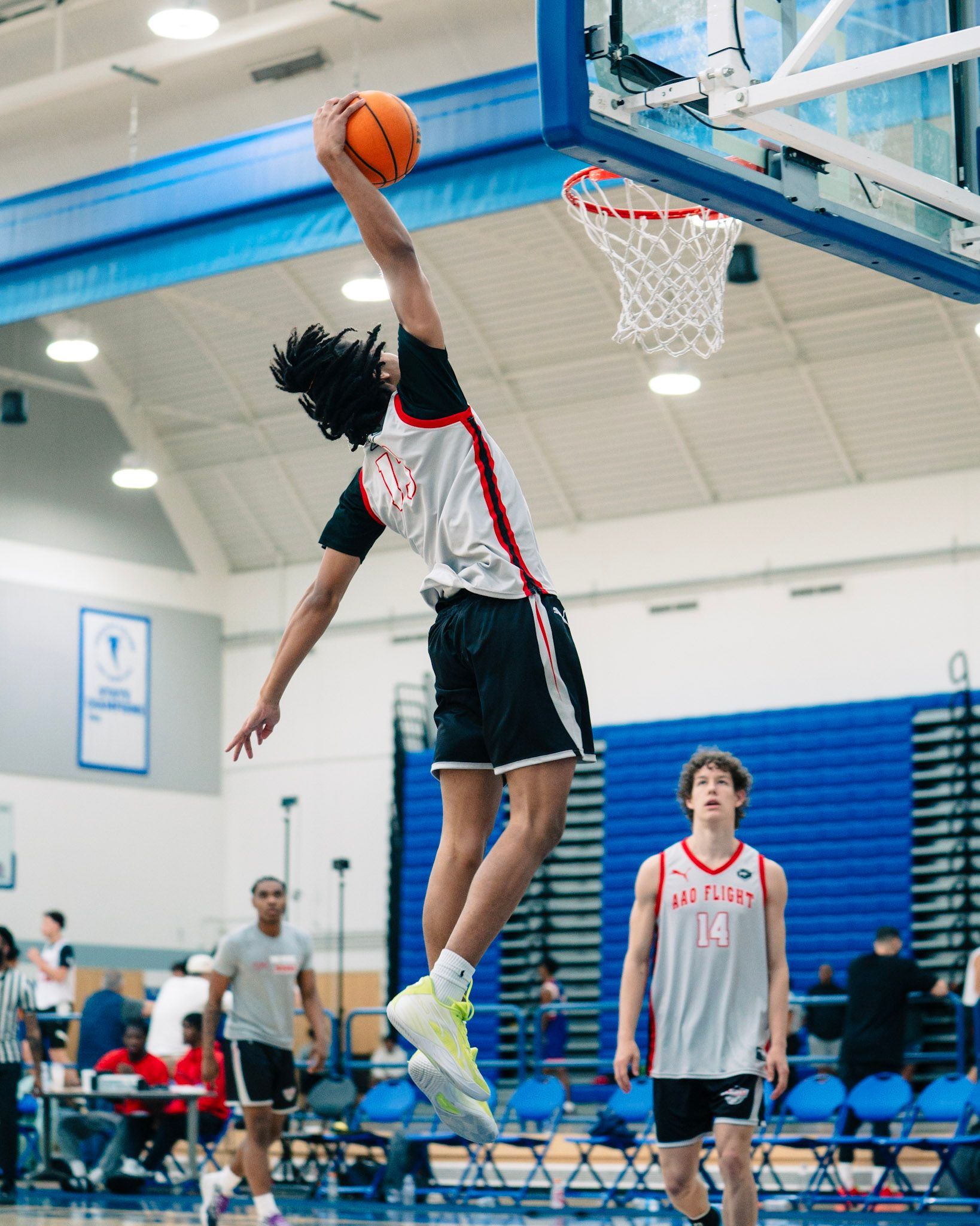 Basketball player dunking the ball, reaching for the basket. Indoor court with a teammate looking on.