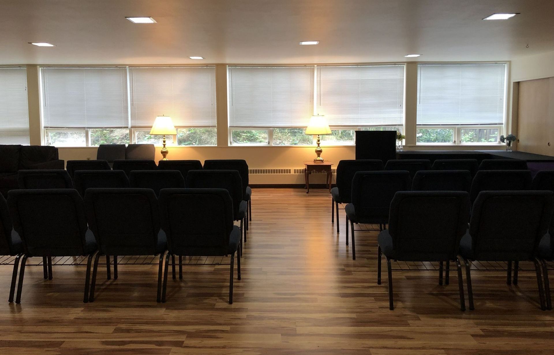 A large room with rows of black chairs and a wooden floor.