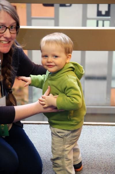 A little boy in a green hoodie is being held by a woman