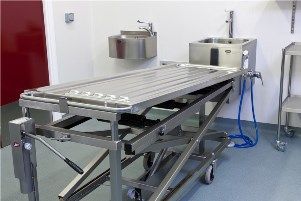 A stainless steel stretcher is sitting in a room next to a sink.