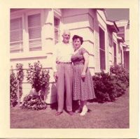 A man and a woman are posing for a picture in front of a house.