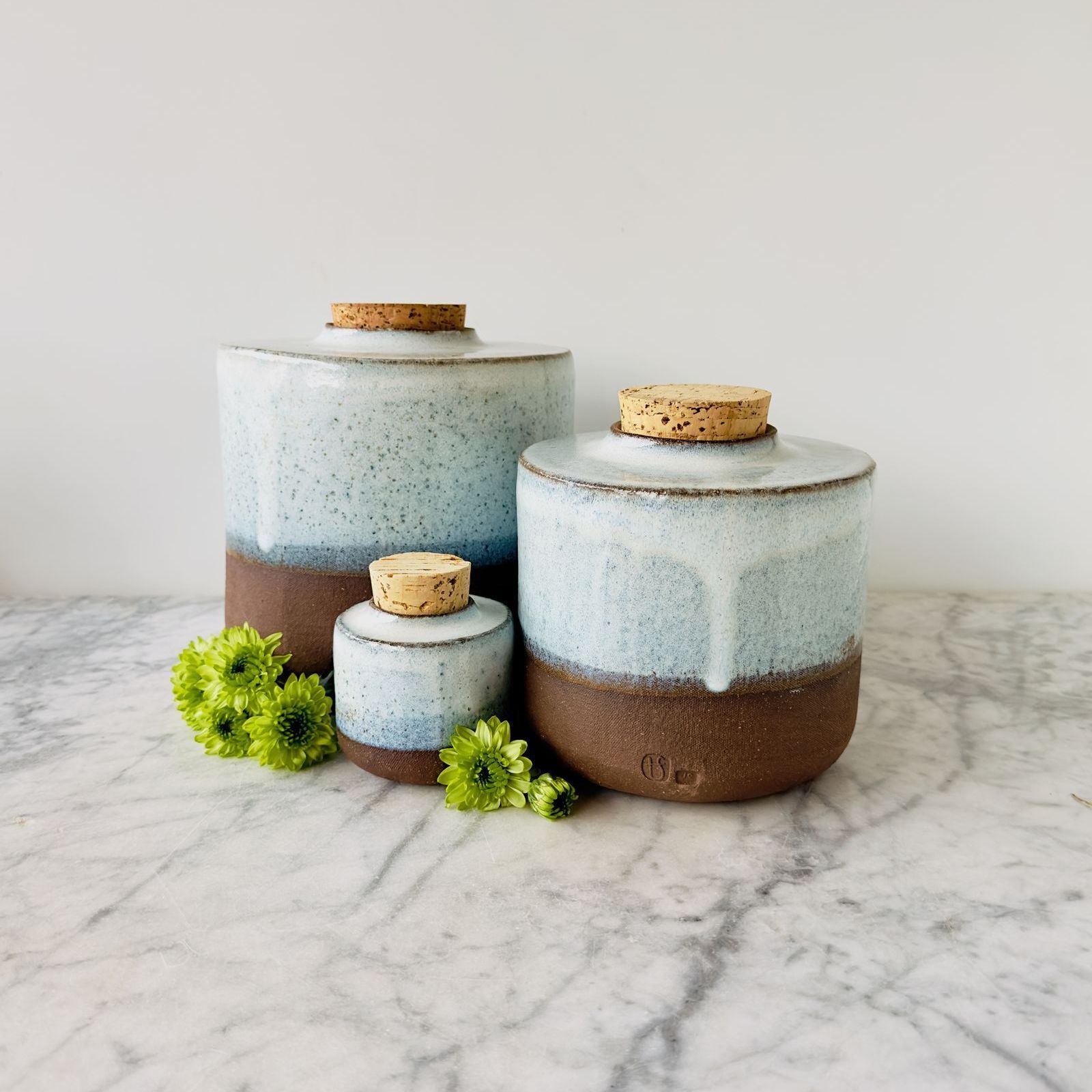 Three ceramic jars with corks are sitting on a marble counter top