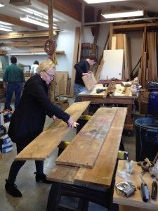 A woman is standing next to a wooden table in a workshop.
