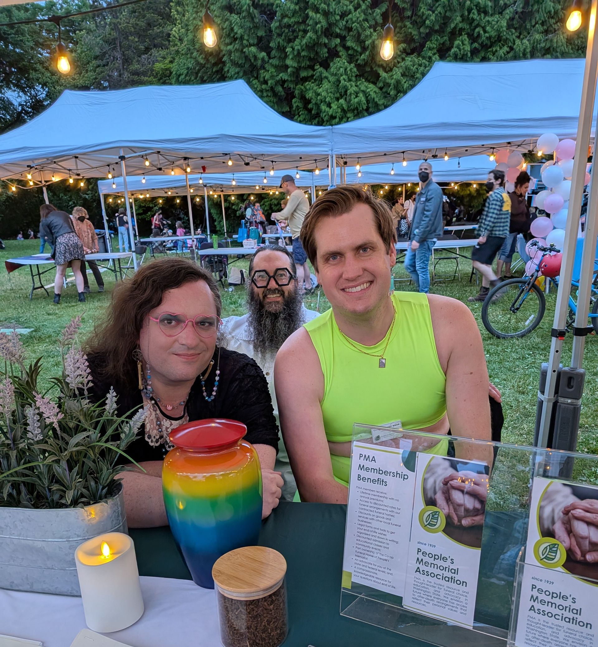 Brendan Dieffenbach, Chris Ronk, Casey Husseman Brandt of People's Memorial Association and The Co-op Funeral Home of Seattle at an outdoor event with marketing materials and a rainbow-patterned urn