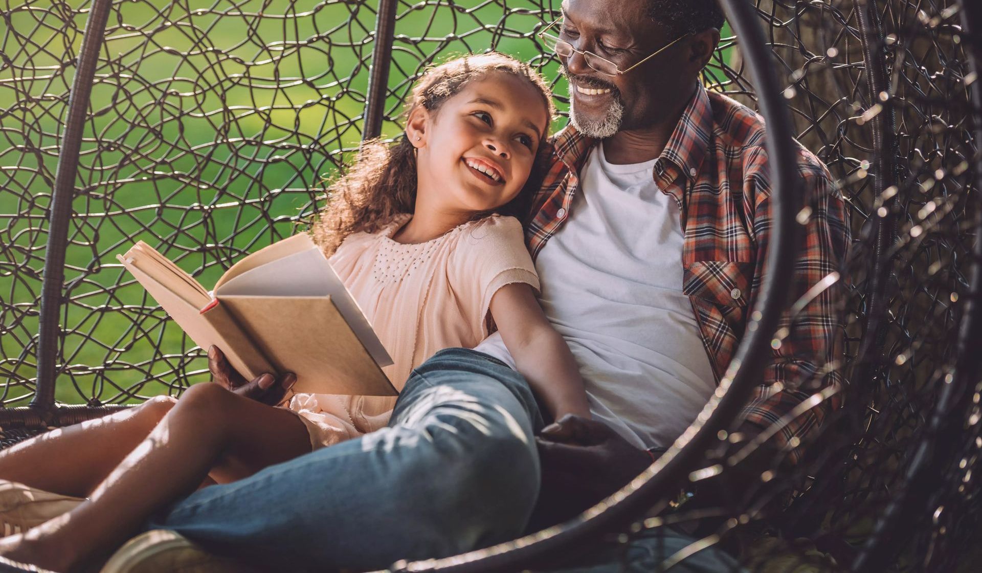 A man and a little girl are sitting in a chair reading a book.