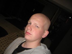 A young man with a shaved head is sitting on a couch