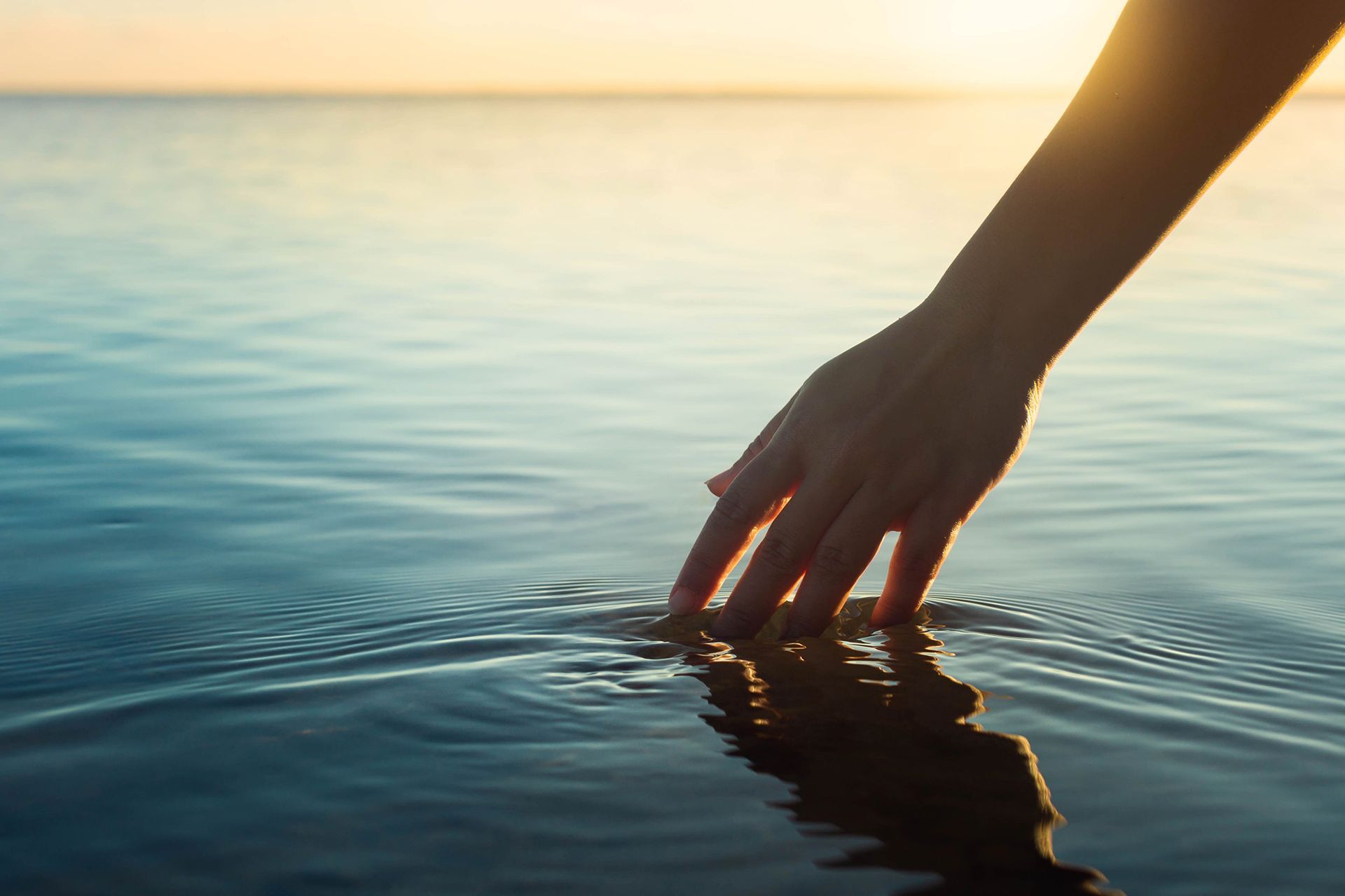 A person 's hand is touching the water in the ocean.