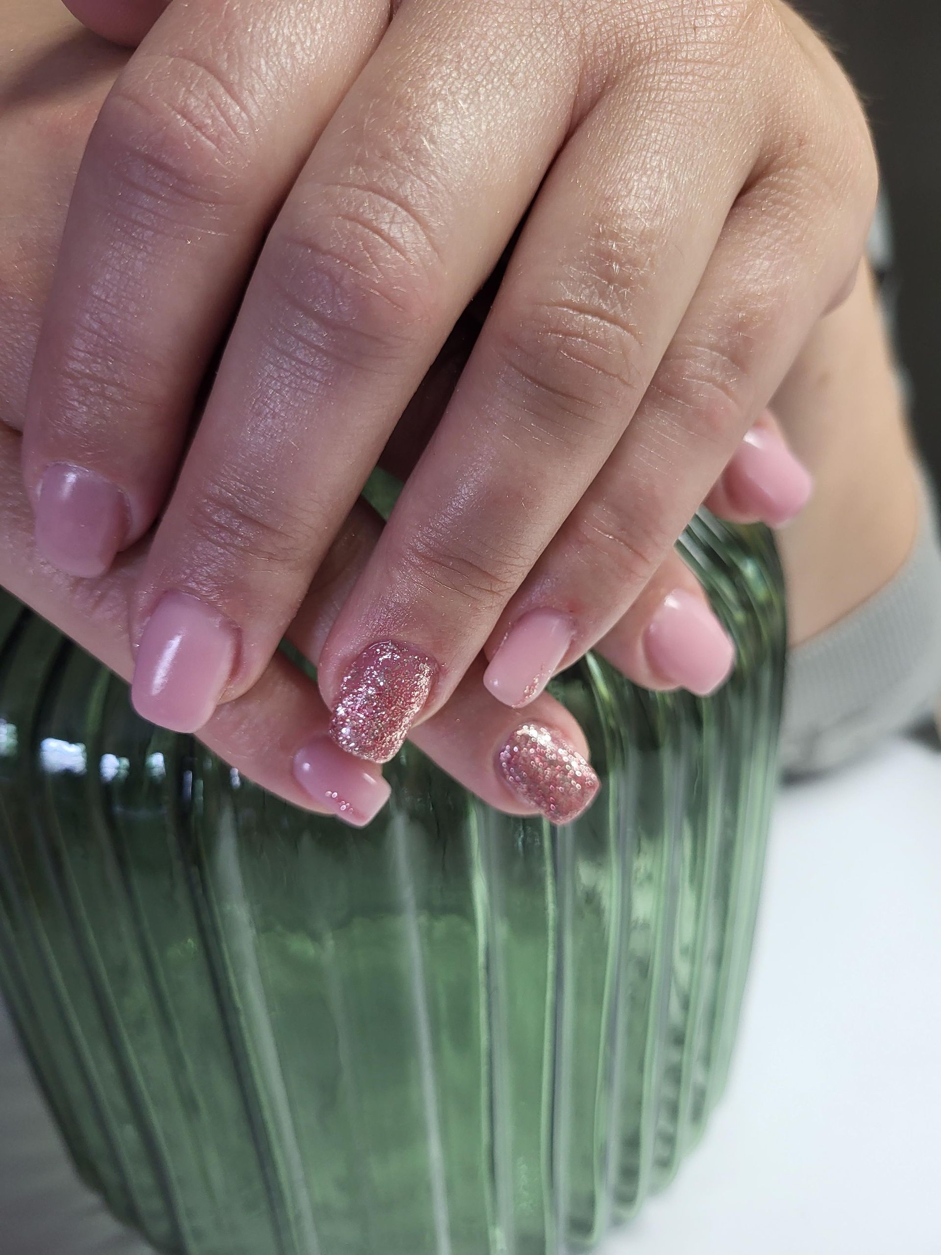 Die Hände einer Frau mit rosa Nägeln halten eine grüne Vase.