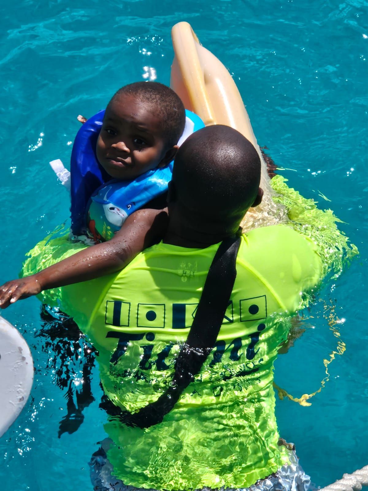 A man in a neon green shirt is holding a child in the water