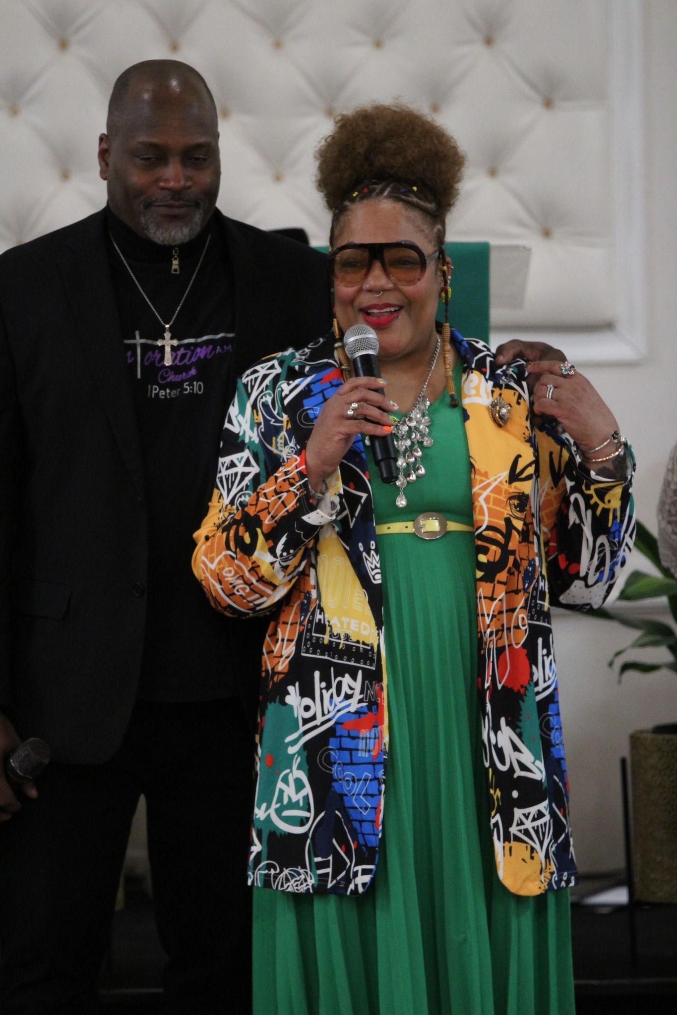 A woman in a green dress is holding a microphone while standing next to a man in a suit.