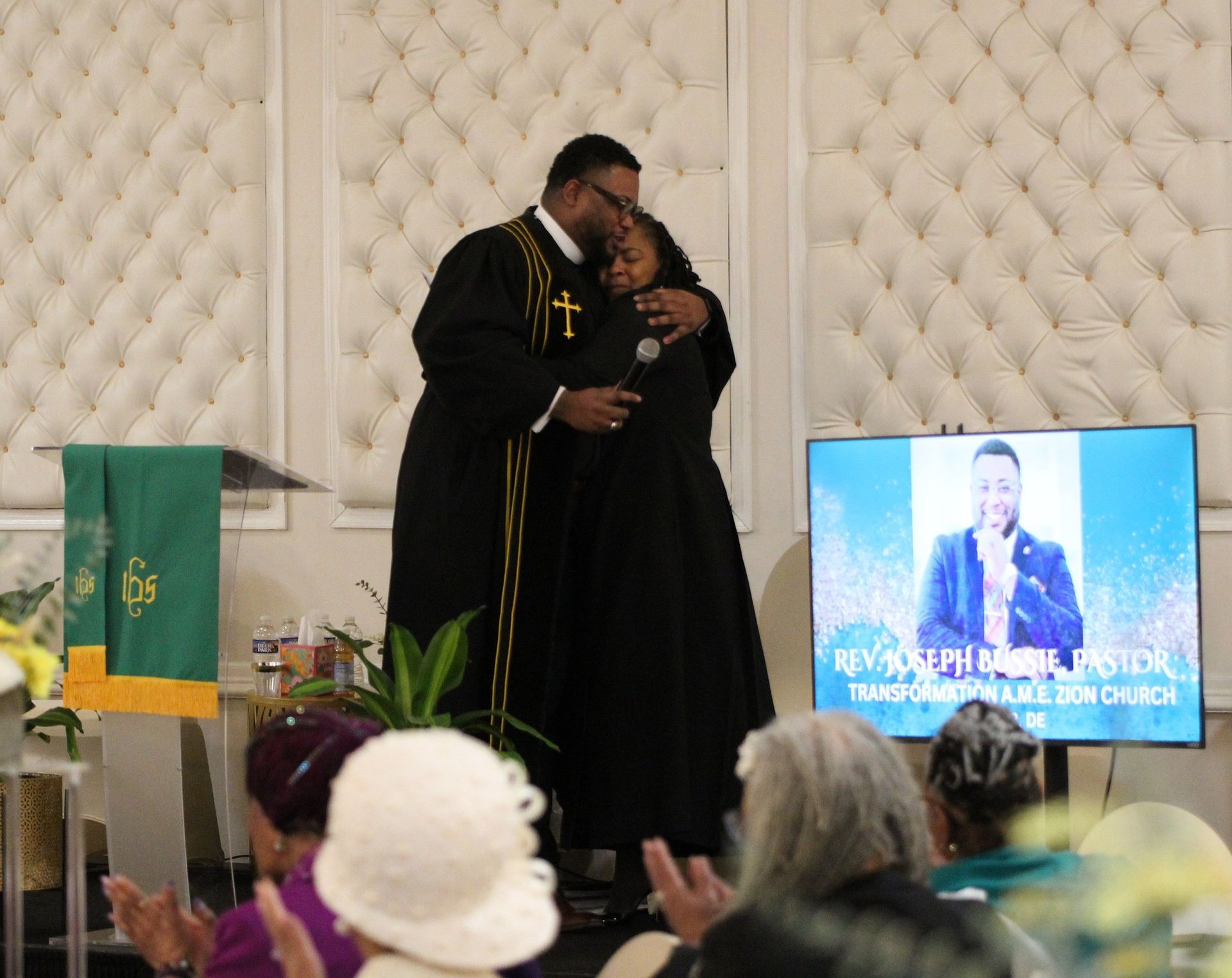A man in a black robe is hugging a woman in front of a crowd