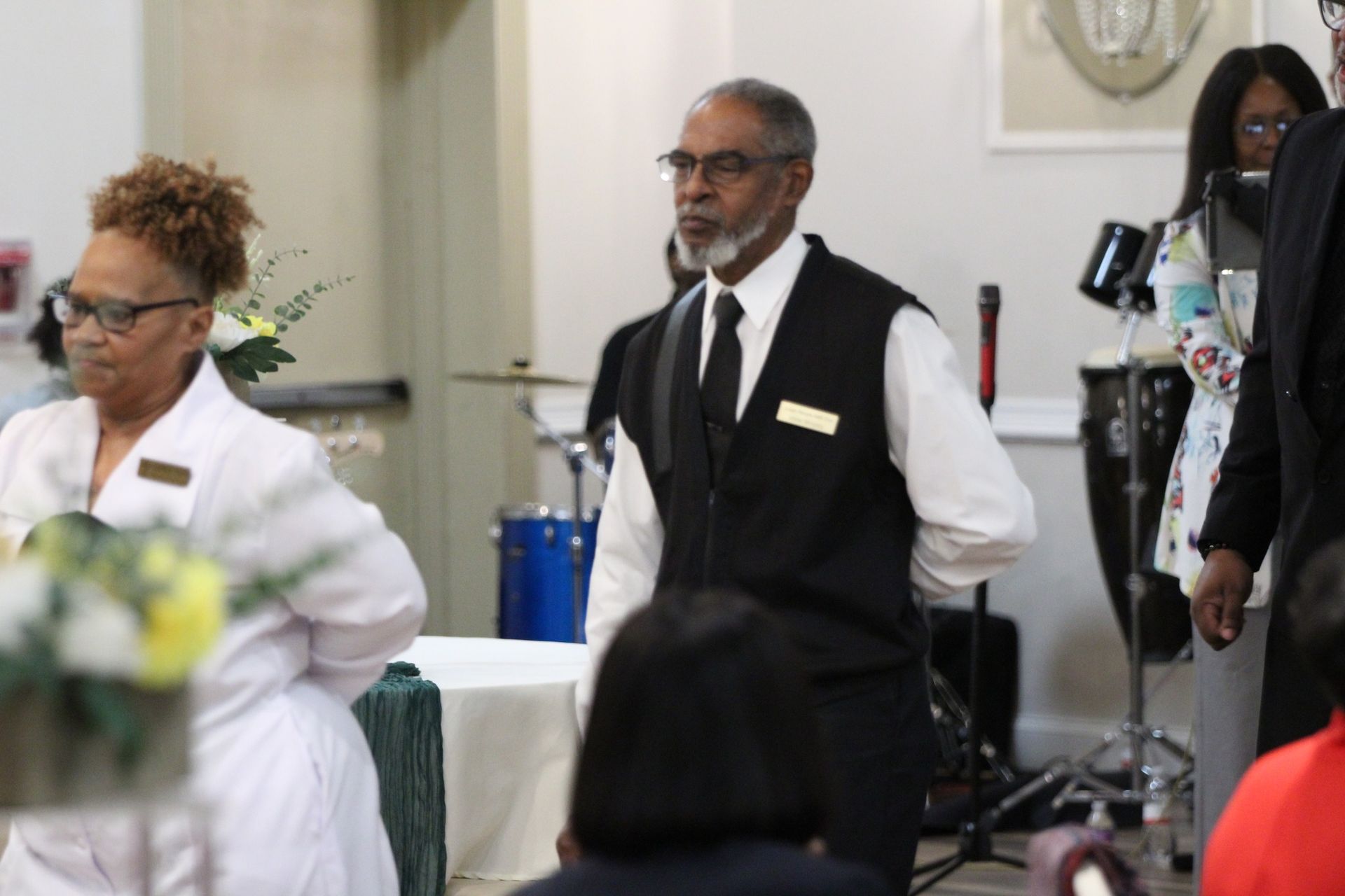 A man in a black vest and tie is standing next to a woman in a white coat