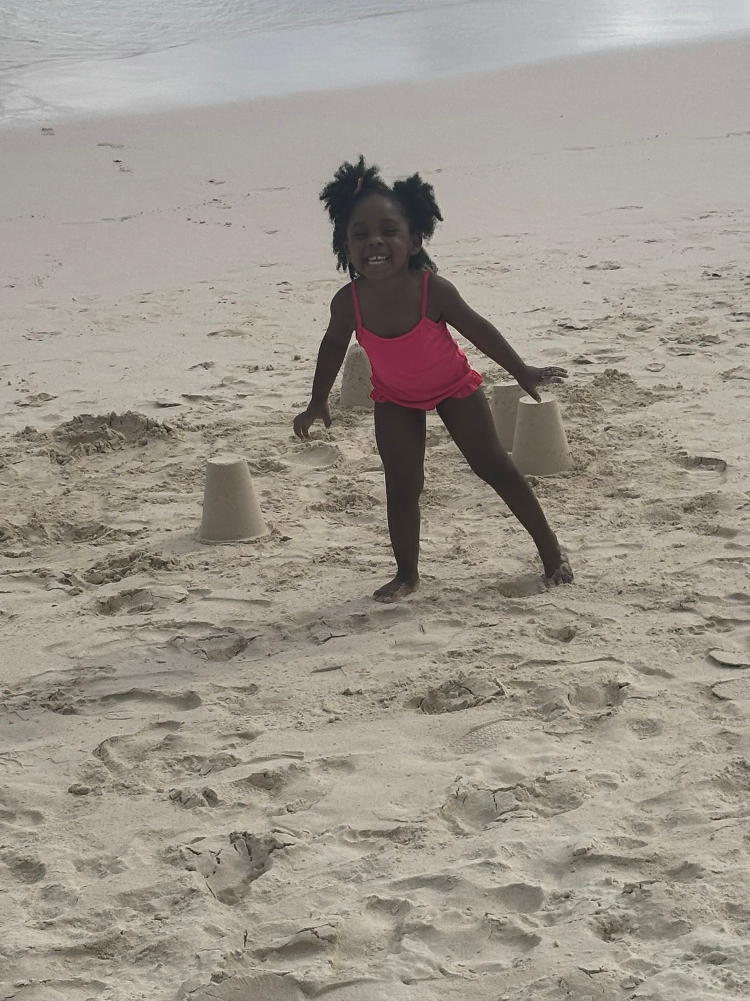 A little girl in a pink bathing suit is playing in the sand on the beach.