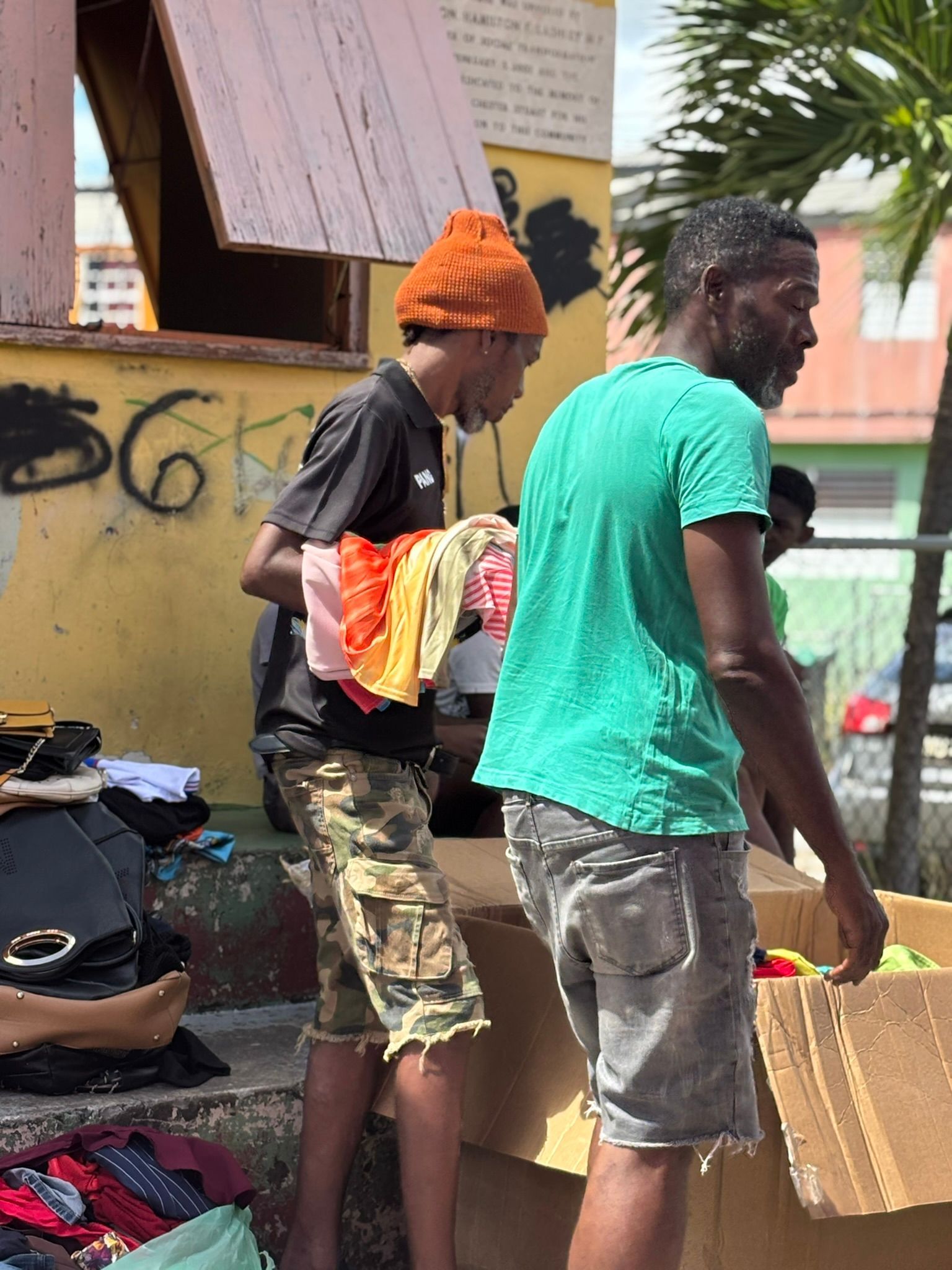 Two men are standing next to each other in front of a yellow building.
