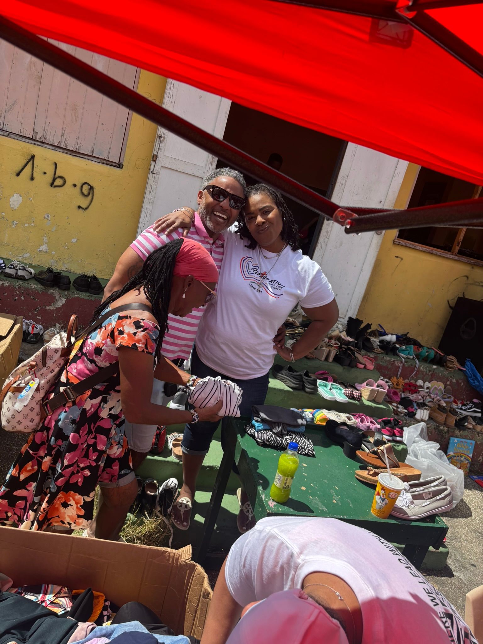 A group of people are standing under a red umbrella at a flea market.