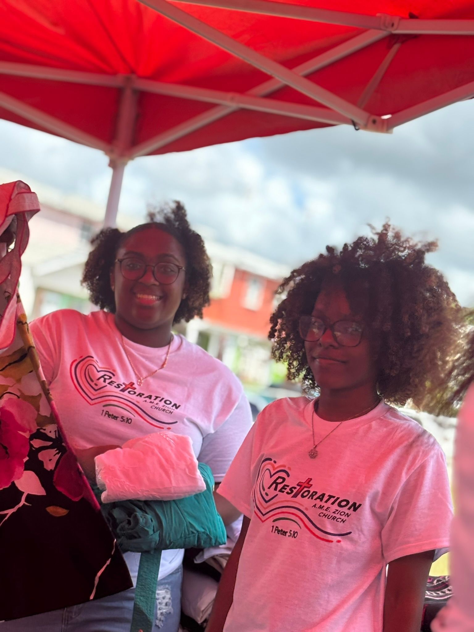 Two women wearing pink shirts are standing under a red umbrella.