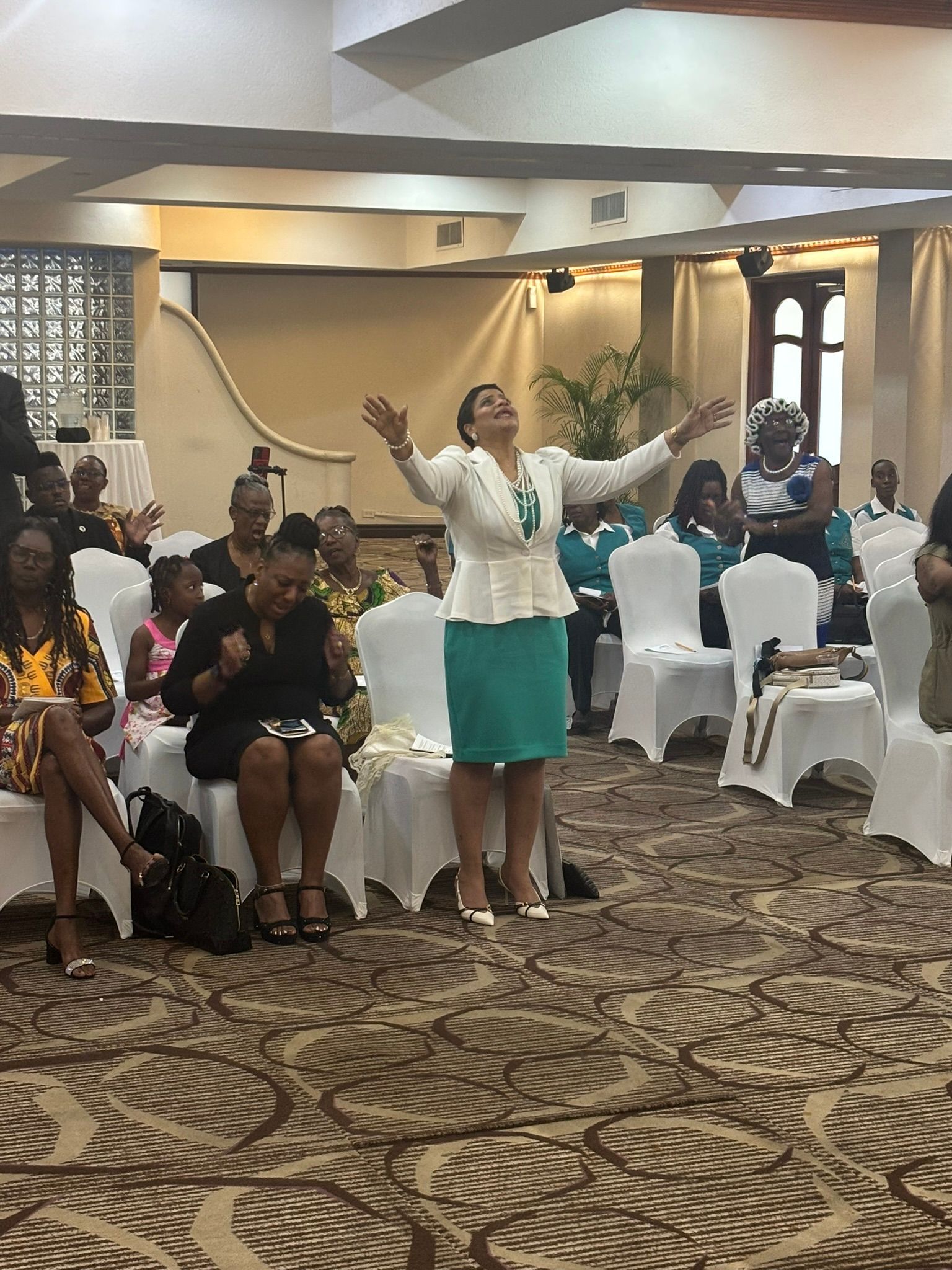 A woman in a green skirt is standing in front of a group of people sitting in chairs.