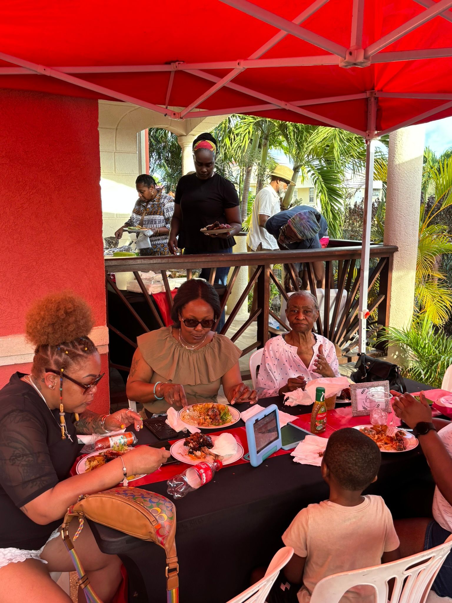 A group of people are sitting at a table eating food under a tent.