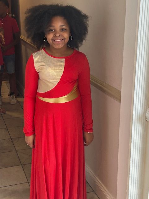 A young girl in a red and gold dress is standing in a hallway.