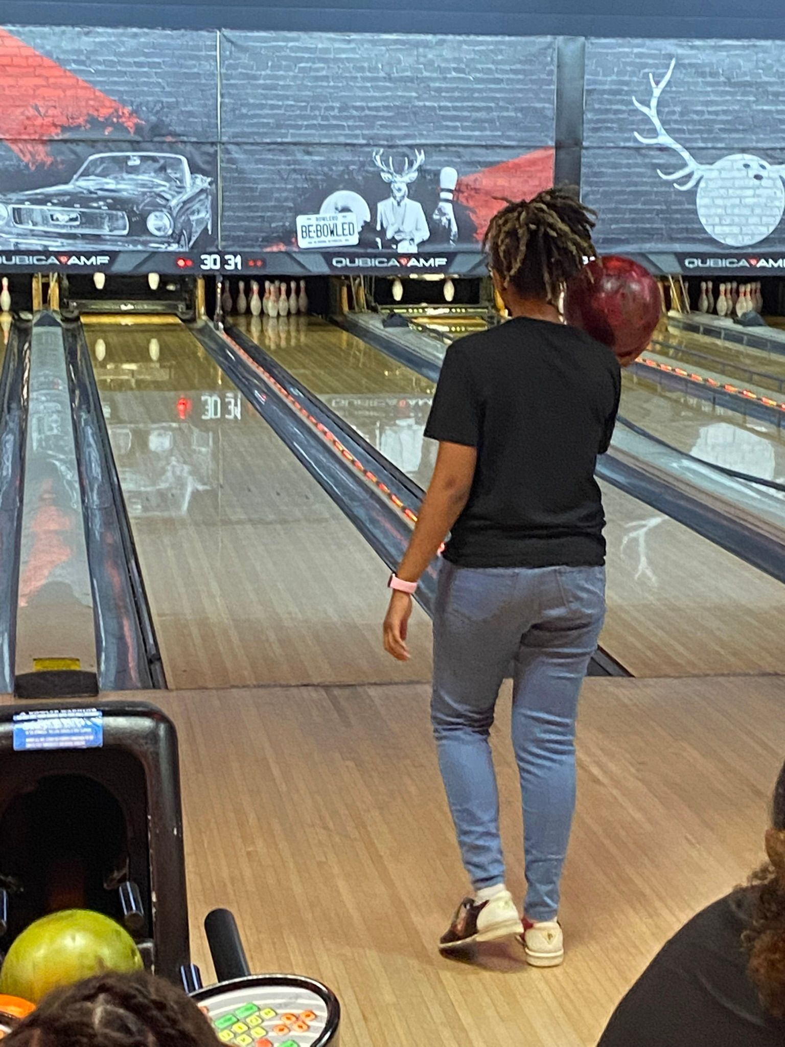 A woman is walking down a bowling alley holding a bowling ball.