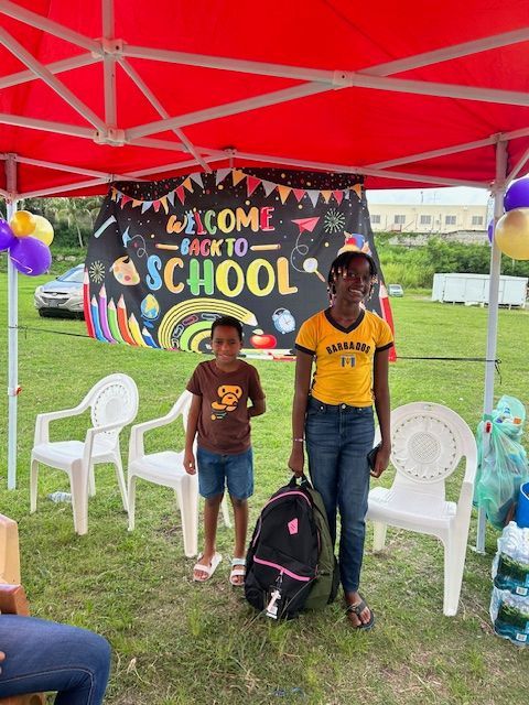 Two children are standing under a tent with a sign that says welcome back to school