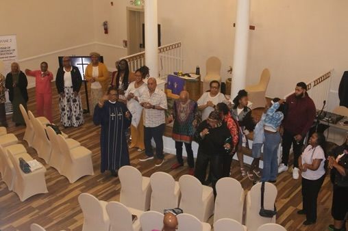 People standing in a church aisle near rows of chairs, some holding children.