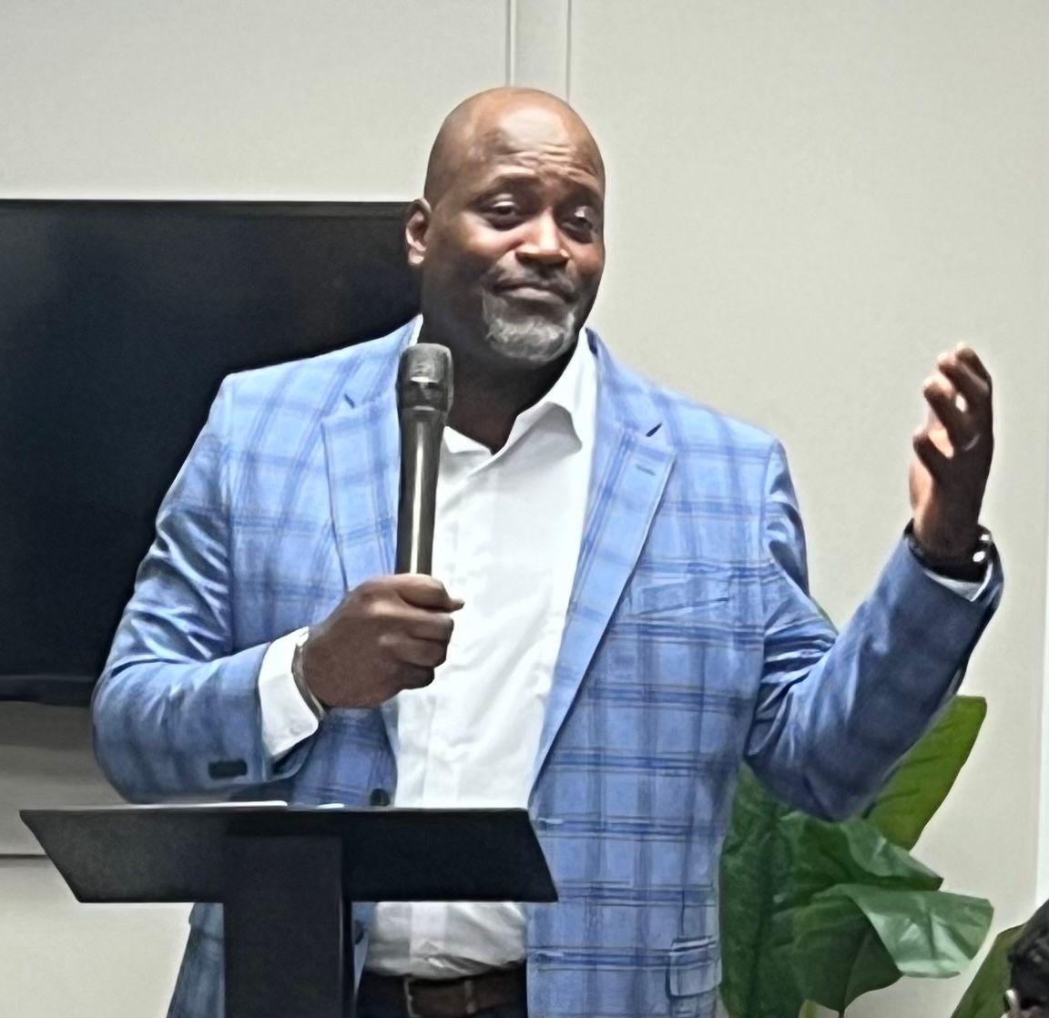 A man in a blue jacket is standing at a podium holding a microphone