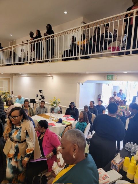 A large group of people are gathered in a room with a balcony