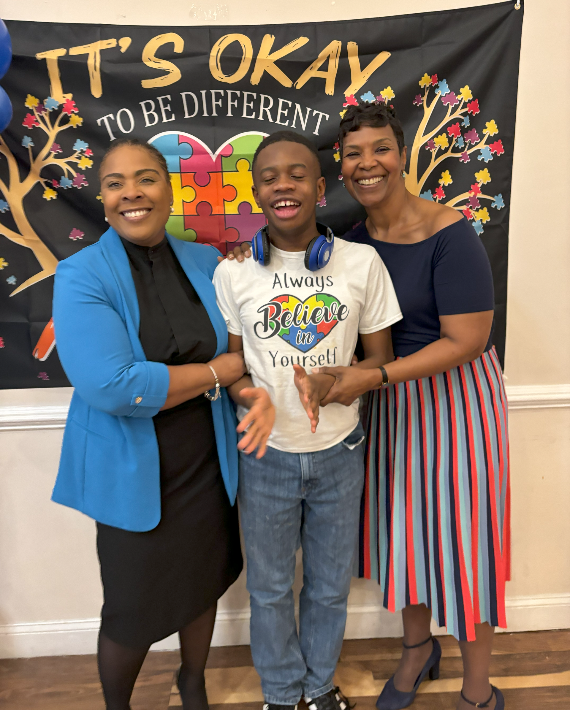 Three people are posing for a picture in front of a banner that says it 's okay to be different