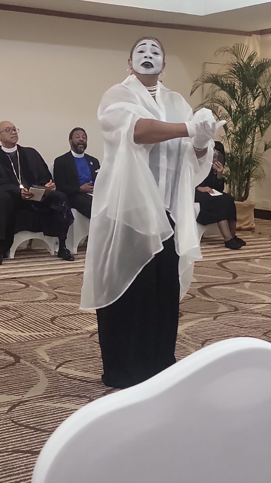 A woman with a white mask on her face is standing in front of a group of people.