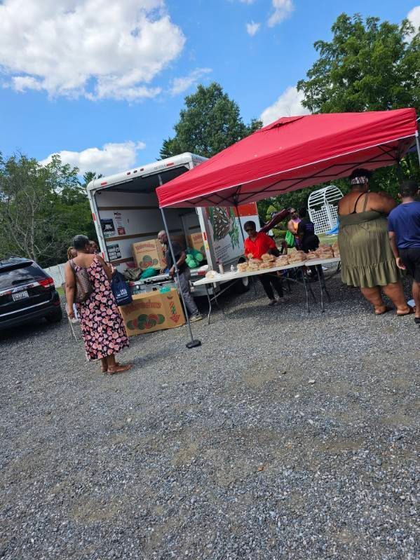A group of people are standing around a table under a red tent in a parking lot.