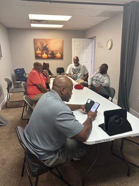 A group of men are sitting around a table and one man is using a tablet