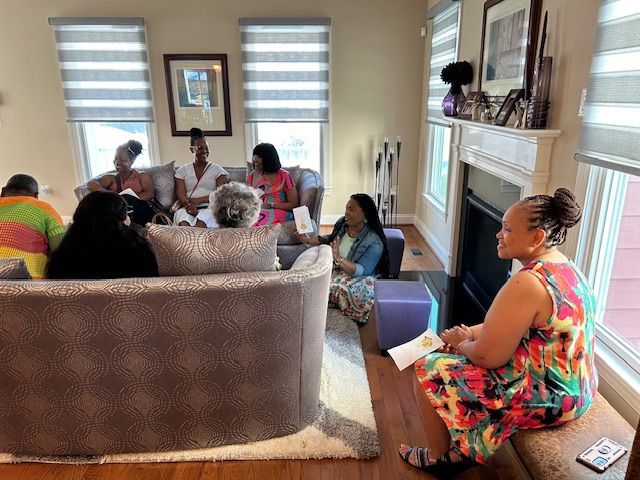 A group of women are sitting around a couch in a living room.