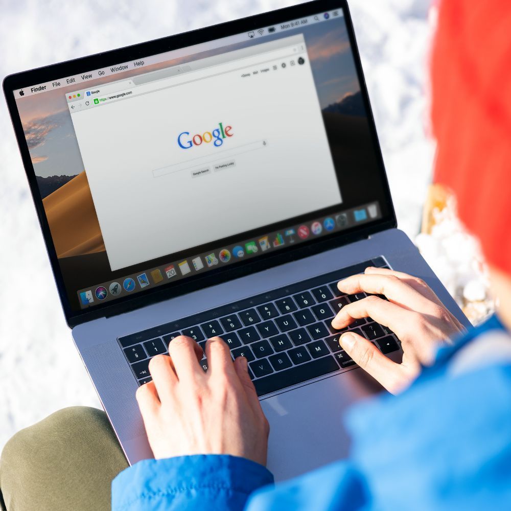 A person is typing on a laptop with google on the screen