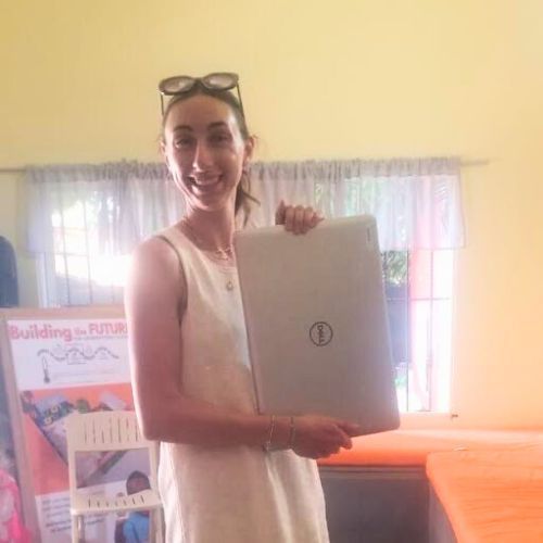 A woman in a white dress is holding a laptop computer.