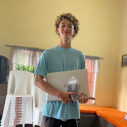 A young man in a blue shirt is holding a laptop in a room.