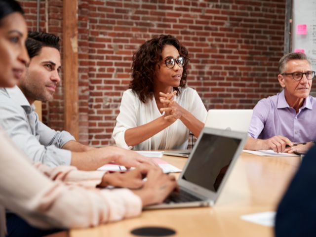 A group of people are sitting around a table with laptops.