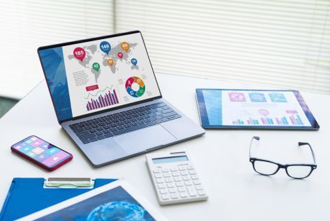 A laptop , calculator , cell phone , tablet and glasses are on a desk.