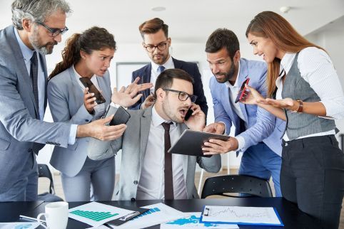 A group of business people are standing around a man talking on a cell phone.