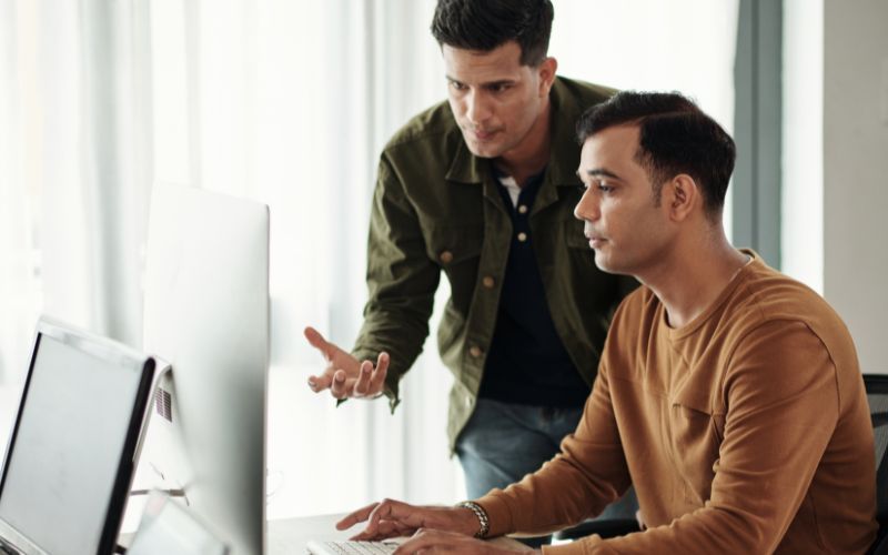 Two men are looking at a computer screen together.