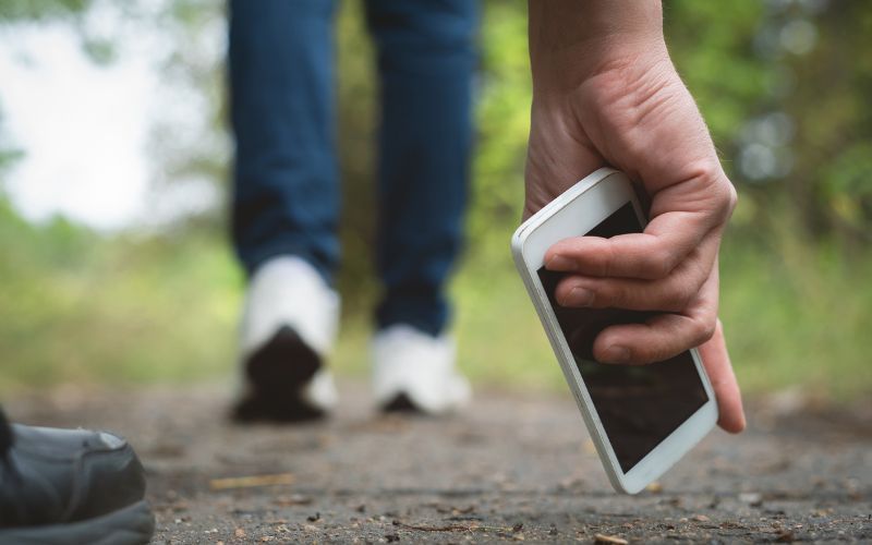 A person is picking up a cell phone from the ground.