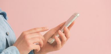 A woman is using a smart phone on a pink background.