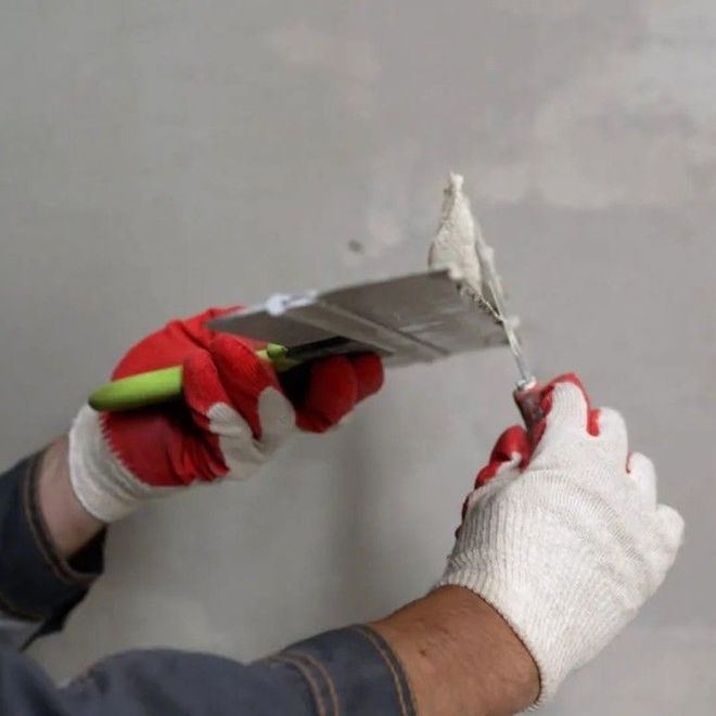Gloved hands using a putty knife to scrape and apply plaster on a wall Gloved hands using a putty knife to scrape and apply plaster on a wall