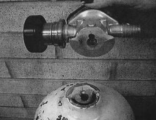 A metal valve detached from a damaged metallic spherical container, likely a pressurized tank.