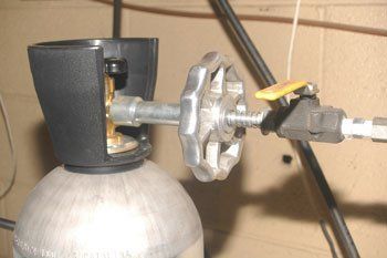 A metal CO2 tank with a hand valve, pressure regulator, and black protective cover.