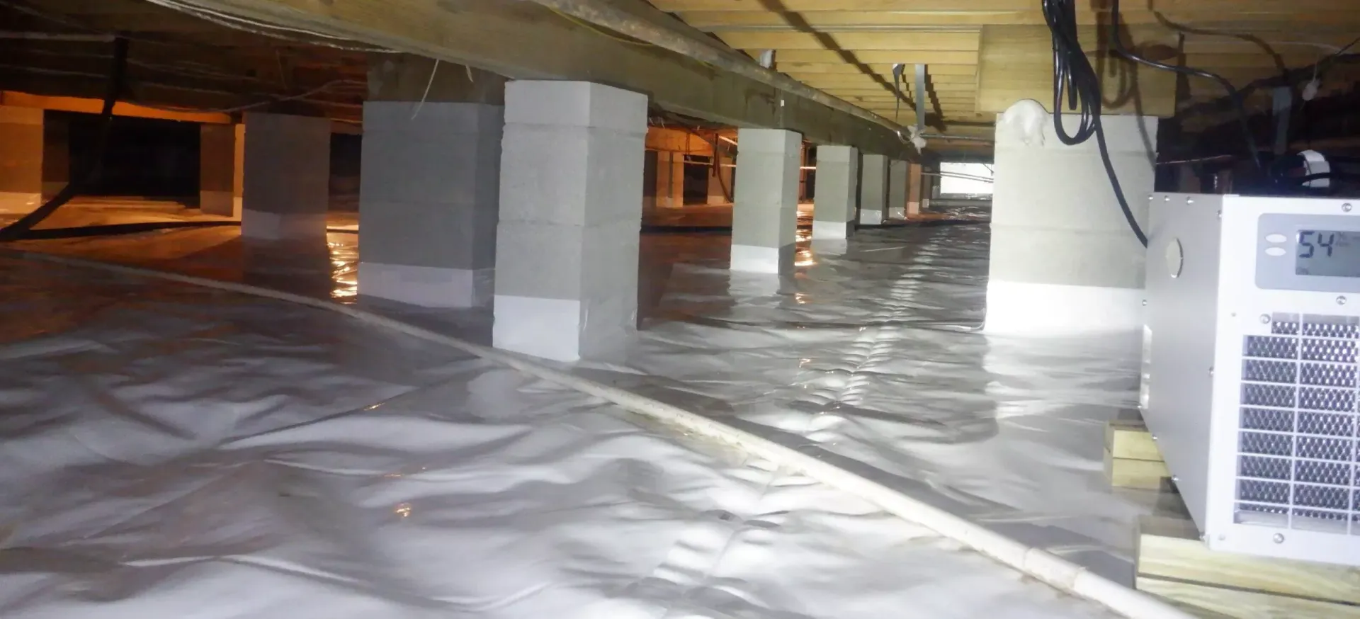 Crawl space with white pillars, plastic ground cover, and equipment.