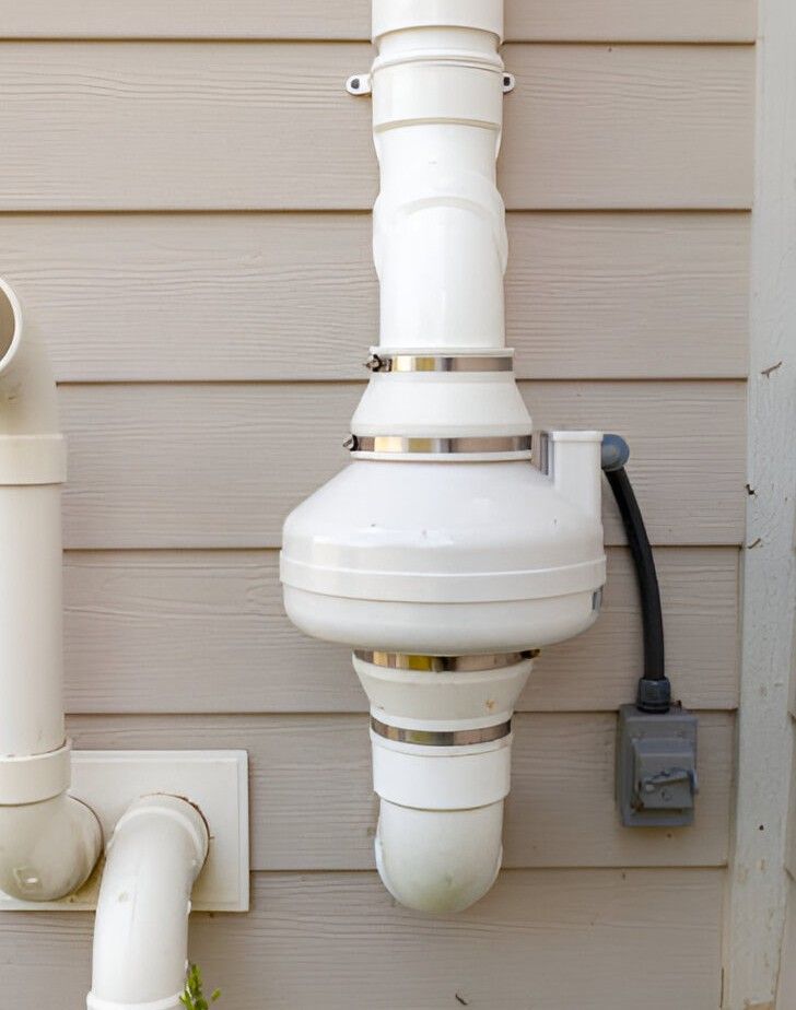 White radon mitigation system pipe on beige siding with electrical box.