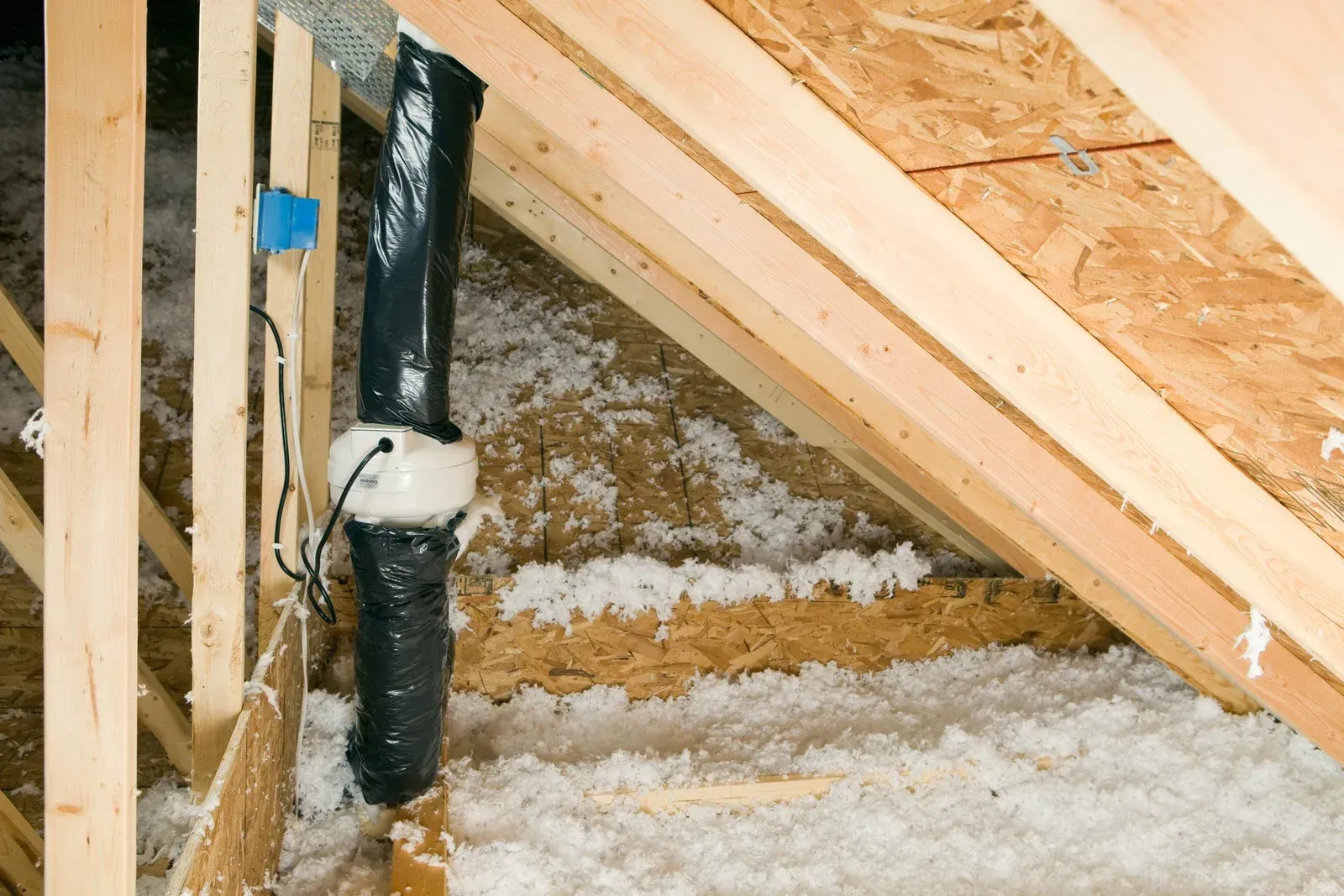 Attic with insulation, wooden beams, and a black, insulated pipe.